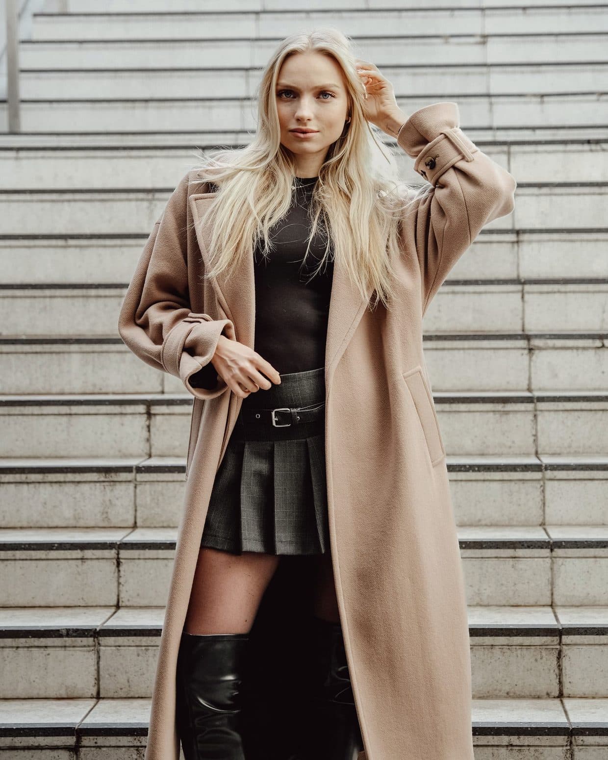Modelo con abrigo largo de lana camel, jersey negro y falda de cuadros, fotografía de moda de calle